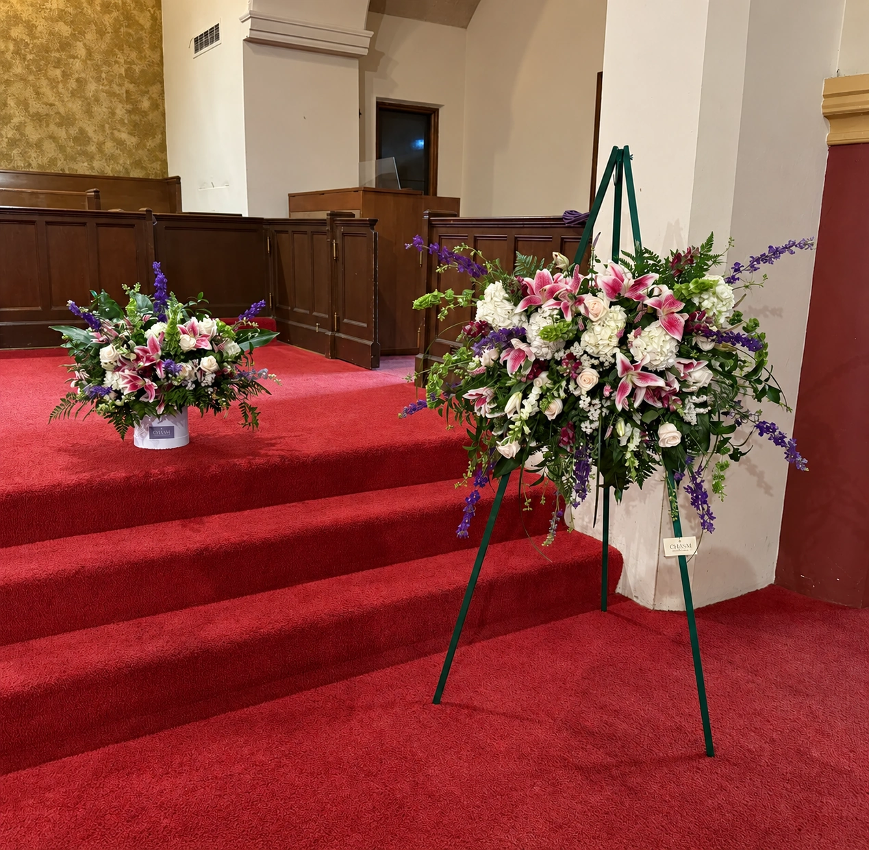 Pink lilies, white roses, and purple flowers arranged beside a gathering space